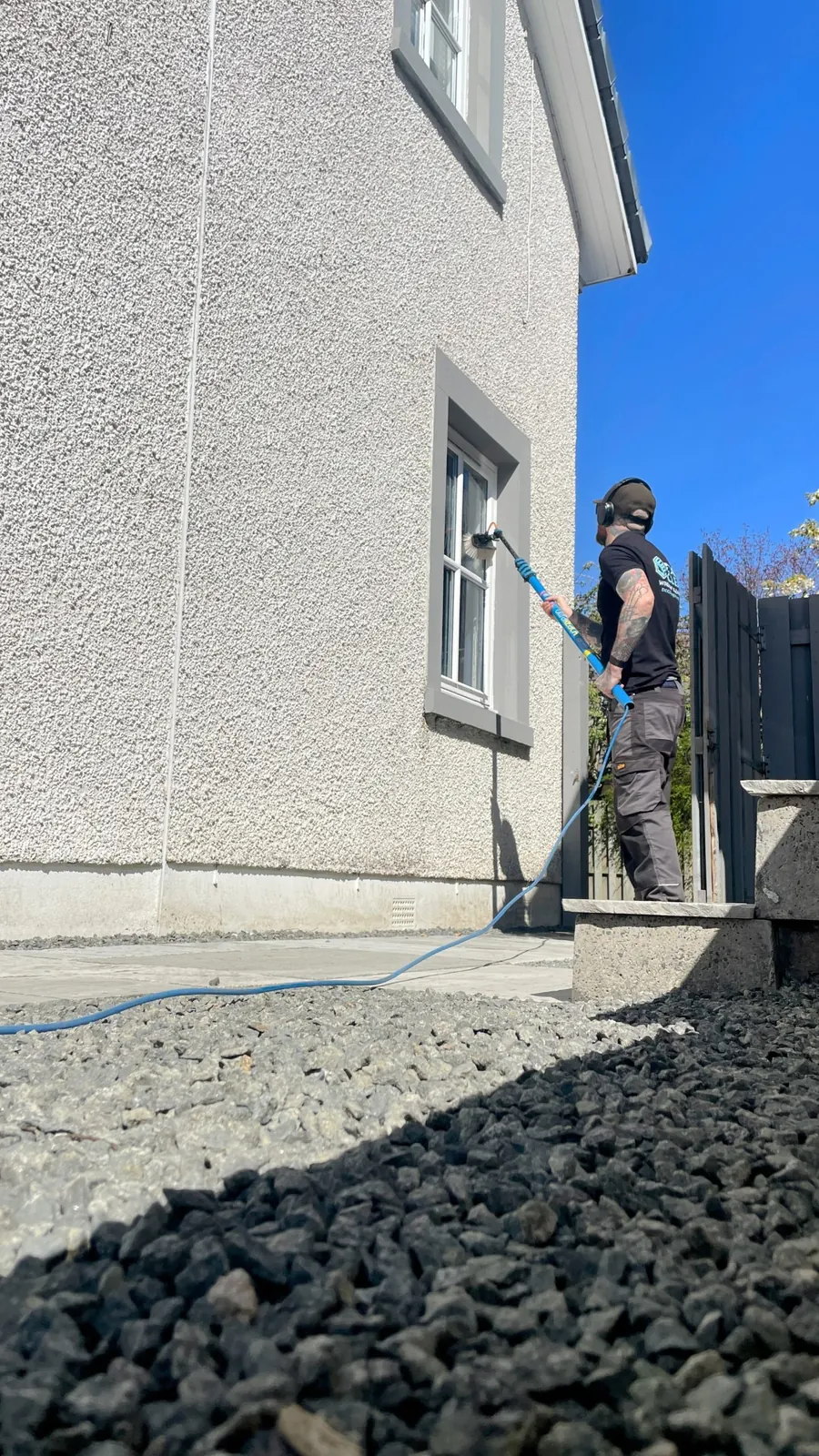 Craig cleaning upstairs windows on a rendered house with a water-fed pole
