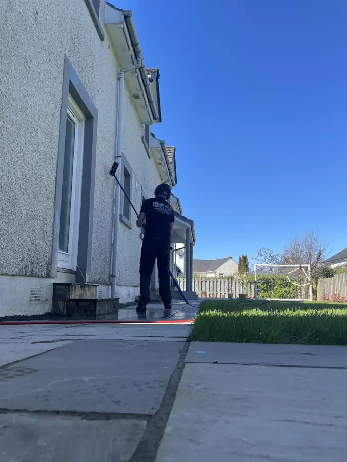 Craig cleaning the windows of a rendered detached house under a blue sky