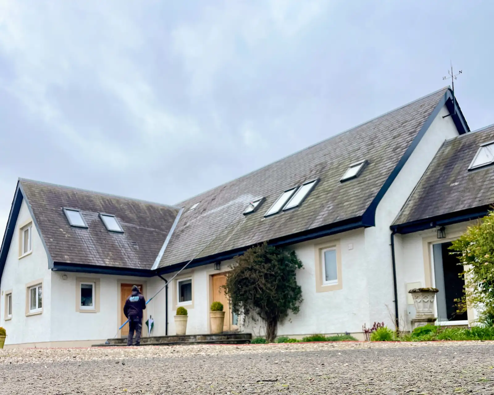 Craig cleaning the windows of a white cottage with a water-fed pole